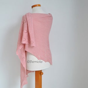 May include: A light pink knitted shawl draped over a mannequin. The shawl features a textured design with openwork detailing along the edges. The fabric is a soft, solid color, and the shawl is displayed against a white background.