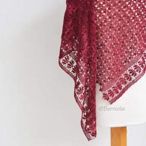 May include: A burgundy crocheted shawl with a delicate lace pattern. The shawl is draped over a white mannequin.