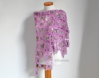 May include: A lilac-coloured, open-weave shawl with colourful floral accents. The shawl is draped over a mannequin, showcasing its intricate crochet design. The floral details are in shades of blue, yellow, and pink.