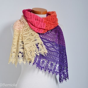 May include: A handmade, open-weave shawl in a gradient of colors, displayed on a mannequin. The shawl transitions from cream to pink, orange, and finally, deep purple. The edges feature a scalloped design, adding a delicate touch to the accessory.