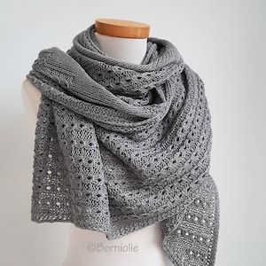 Könnte beinhalten: Ein grauer Strick-Schal mit einem zarten Lochmuster. Der Schal ist über eine Schaufensterpuppe gelegt.