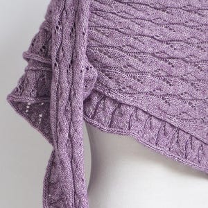 Könnte beinhalten: Ein lavendelfarbener Strickschal mit detailliertem Lochmuster. Der Schal hat ein strukturiertes Muster und einen gewellten Rand. Der Stoff ist über einer Form drapiert und zeigt die komplizierte Strickarbeit und die sanfte Farbe.