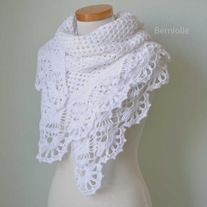 May include: A white, crocheted shawl with a delicate, lacy design. The shawl is draped over a mannequin, showcasing its intricate floral and geometric patterns. The edges feature a scalloped trim, adding a touch of elegance. The word "Berniolie" is visible on the right side.