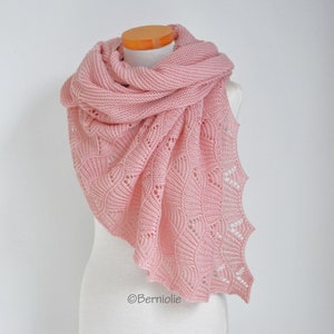 May include: A delicate pink knitted shawl with a lacy pattern. The shawl is draped over a white mannequin.
