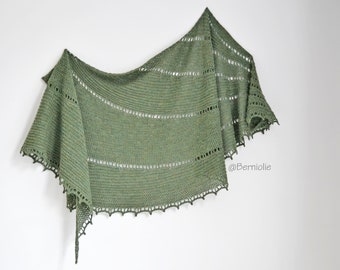 May include: A green crocheted shawl with a lacy border. The shawl is draped over a white wall. The text "@Berniolie" is visible in the lower right corner of the image.
