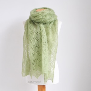 Könnte beinhalten: Ein hellgrüner gestrickter Spitzen-Schal mit einem zarten Muster. Der Schal ist über eine weiße Schaufensterpuppe gelegt.