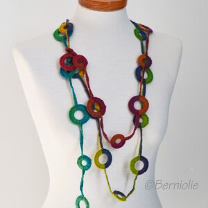 Op de afbeelding: Een veelkleurige gehaakte ketting met grote, kleurrijke cirkels. De ketting is gemaakt van garen in tinten groen, blauw, rood en paars.