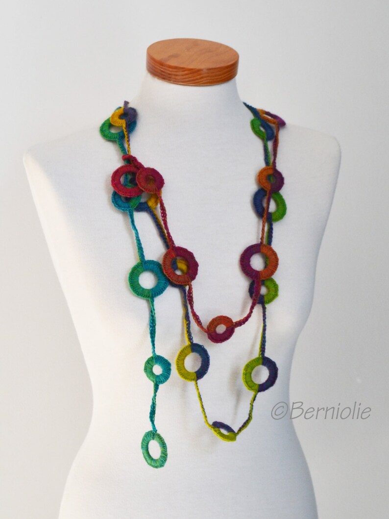 Op de afbeelding: Een veelkleurige gehaakte ketting met grote, kleurrijke cirkels. De ketting is gemaakt van garen in tinten groen, blauw, rood en paars.