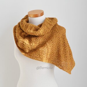 Könnte beinhalten: Ein senfgelber gestrickter Schal mit einem strukturierten Muster. Der Schal ist über eine weiße Schaufensterpuppe gelegt.