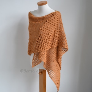 Op de afbeelding: Een handgemaakte, open geweven sjaal in een warme, aardse oranje tint. De sjaal heeft een textuur, bobbelachtig patroon en een gedrapeerd ontwerp. Het item wordt op een mannequin getoond, waarbij de vorm en stijl worden getoond. Een veelzijdig accessoire.