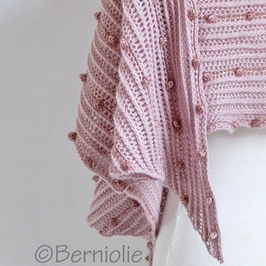 May include: A pink crocheted shawl with a textured pattern and small beads along the edges.