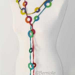 Op de afbeelding: Een kleurrijke gehaakte ketting met een lange streng van verbonden cirkels. De ketting wordt getoond op een wit mannequin.