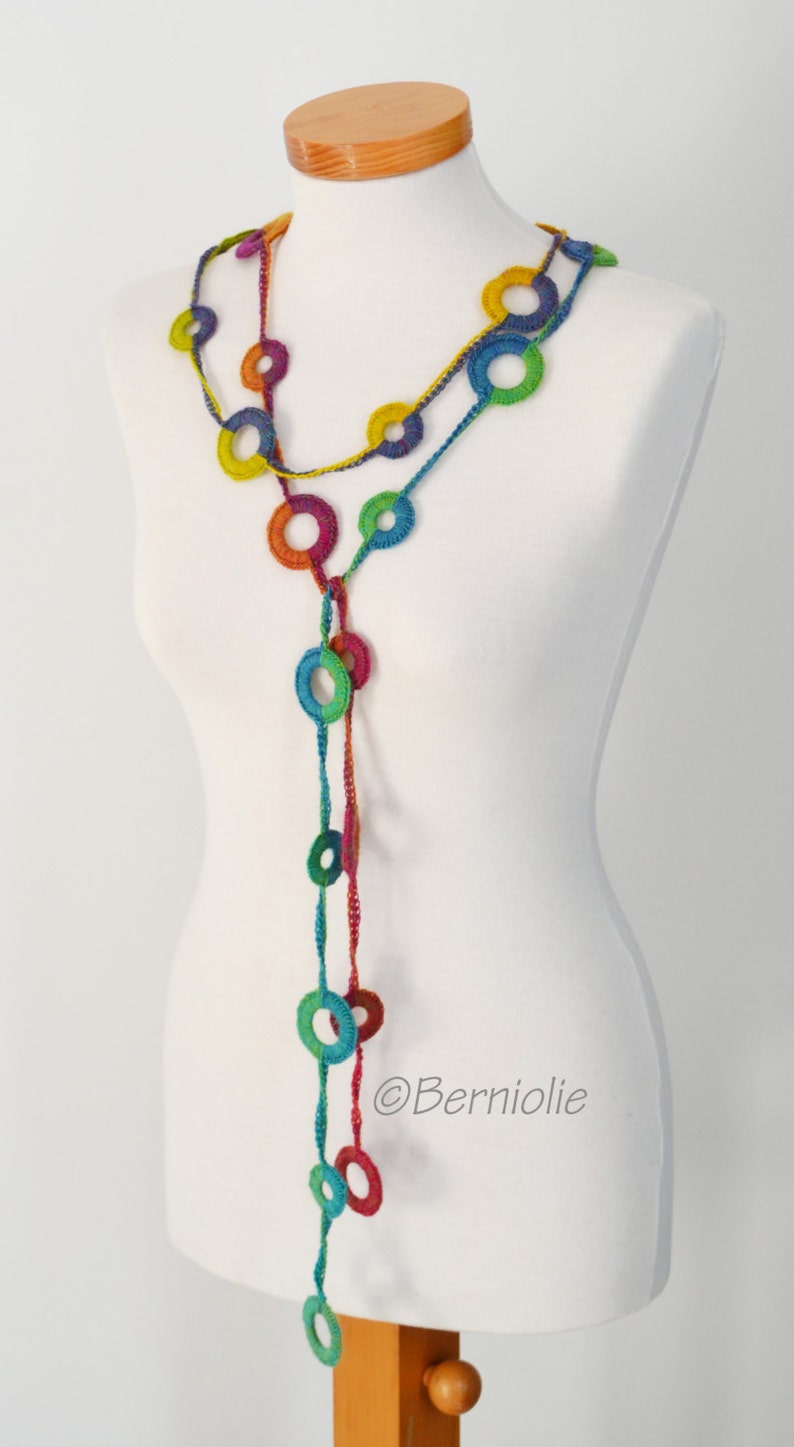 Op de afbeelding: Een kleurrijke gehaakte ketting met een lange streng van verbonden cirkels. De ketting wordt getoond op een wit mannequin.