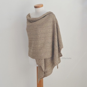 Può includere: Uno scialle lavorato a maglia color beige, drappeggiato su un manichino. Lo scialle presenta un motivo strutturato con linee orizzontali e un design drappeggiato. Il tessuto appare morbido e leggero, adatto alla stratificazione. Lo scialle è esposto su sfondo bianco.