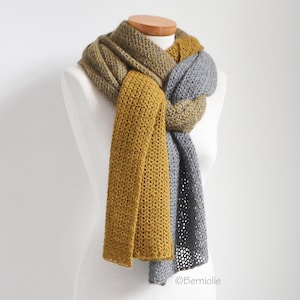 May include: A handmade scarf in shades of mustard yellow, gray, and olive green, displayed on a mannequin. The scarf has a textured, open weave design. The scarf is knotted in the front, with the ends hanging down. The scarf is a cozy accessory.