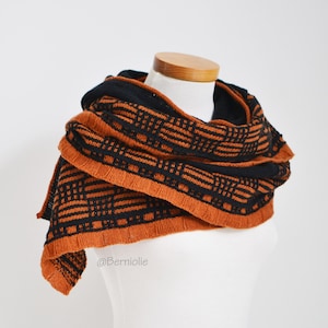 May include: A brown and black knitted scarf with a geometric pattern. The scarf is draped over a white mannequin.