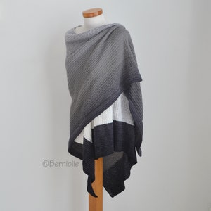 May include: A gray and black shawl with a textured pattern is draped over a mannequin. The shawl features a gradient effect, transitioning from light gray at the top to dark gray and black at the bottom. The bottom edge has a striped design.