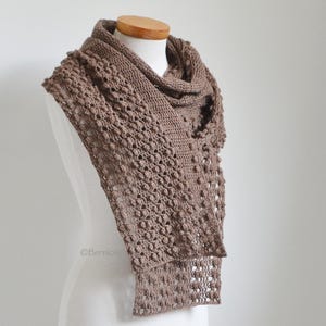Può includere: Sciarpa marrone all'uncinetto fatta a mano, esposta su un manichino. La sciarpa presenta un design testurizzato a punto nocciola e una forma rettangolare. Il colore è un marrone tenue e la sciarpa è drappeggiata per mostrare la sua lunghezza e consistenza.