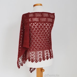 Peut inclure: Un châle en crochet bordeaux présenté sur un mannequin. Le châle présente un motif ajouré et un bord festonné. La texture et la couleur sont mises en valeur, soulignant la qualité artisanale du vêtement. Le châle est drapé pour mettre en valeur sa forme.