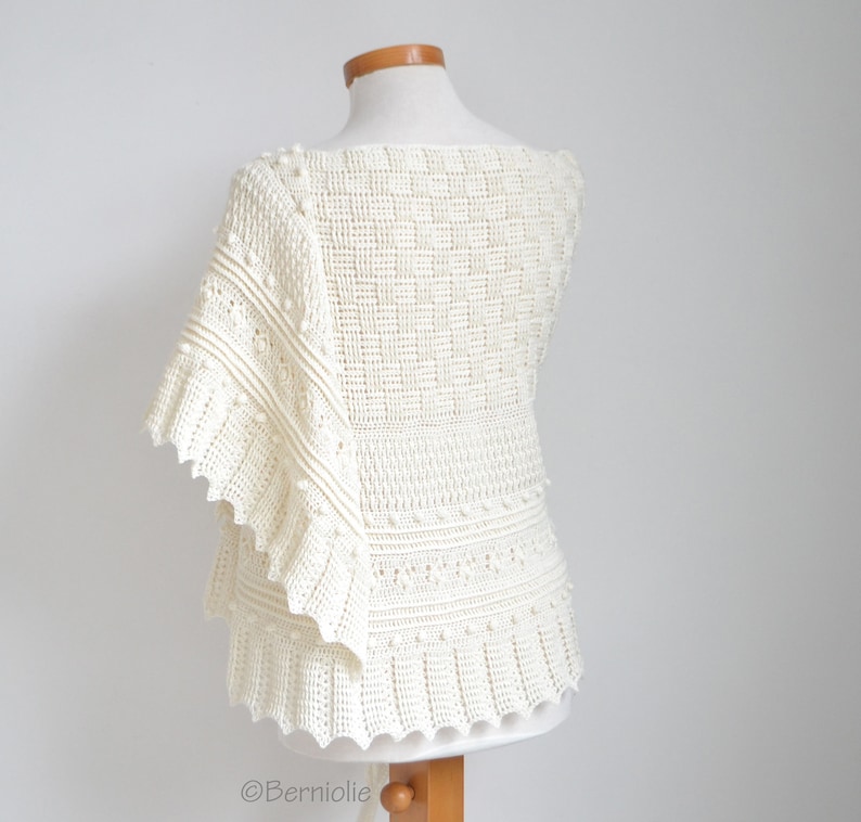 May include: An off-white crochet top featuring a square neckline and a complex textured pattern. The garment displays a combination of grid-like stitches, horizontal bands, and small raised bobbles, with a wide, ruffled sleeve detail.