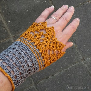 May include: Grey and mustard yellow crocheted wrist warmers with a lacy design. The wrist warmers are made with a delicate stitch pattern and have a contrasting colour border.