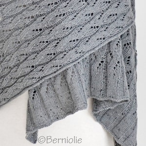 May include: A gray knitted shawl with a delicate lace pattern. The shawl is folded in half and draped over a white surface. The text "©Berniolie" is visible in the lower right corner of the image.
