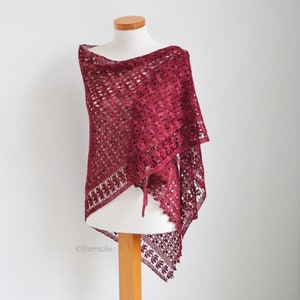 Könnte beinhalten: Ein bordeauxfarbener Schal mit offener, durchbrochener Webart wird auf einer Schaufensterpuppe präsentiert. Der Schal hat ein zartes Blumenmuster an den Rändern und einen gewellten Saum. Ein Kordelverschluss ist sichtbar. Der Schal ist zum Überwerfen der Schultern gedacht.