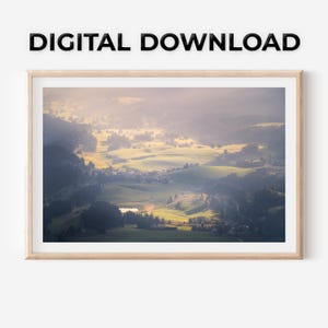 Può includere: Una stampa incorniciata di un paesaggio di valle con dolci colline verdi, un piccolo villaggio e un lago. L'immagine è immersa in una morbida luce solare, creando un'atmosfera calda e invitante. Il testo "DIGITAL DOWNLOAD" è in alto.