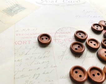 May include: A collection of brown wooden buttons with two holes each. The buttons are scattered on a white surface with handwritten text.