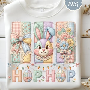 May include: White sweatshirt featuring a colorful Easter design. The design includes three rectangular panels with a bunny, flowers, and bows. The word "HOP HOP" is written below the panels with Easter egg and carrot accents.