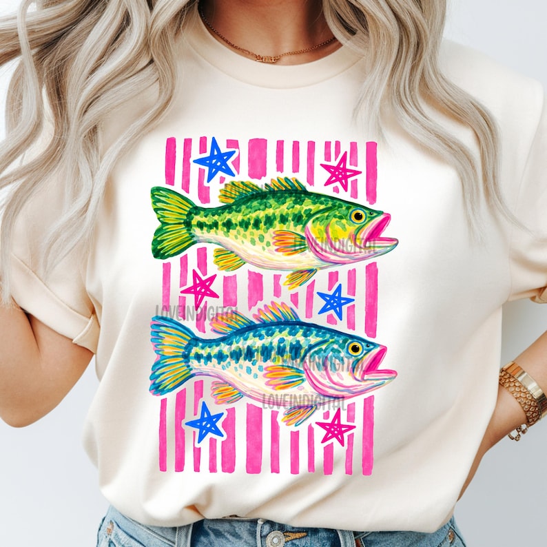 May include: Cream-colored t-shirt featuring a watercolor design of two fish, one green and one blue, set against a pink striped background with blue and pink stars. The text "LOVEINDIGITAL" is visible on the design.