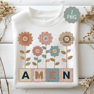 May include: White sweatshirt featuring a floral design with the word "AMEN" in patchwork letters. The flowers are in shades of brown, pink, and blue, with green stems and leaves. A small, green "1 PNG" graphic is in the upper right corner.
