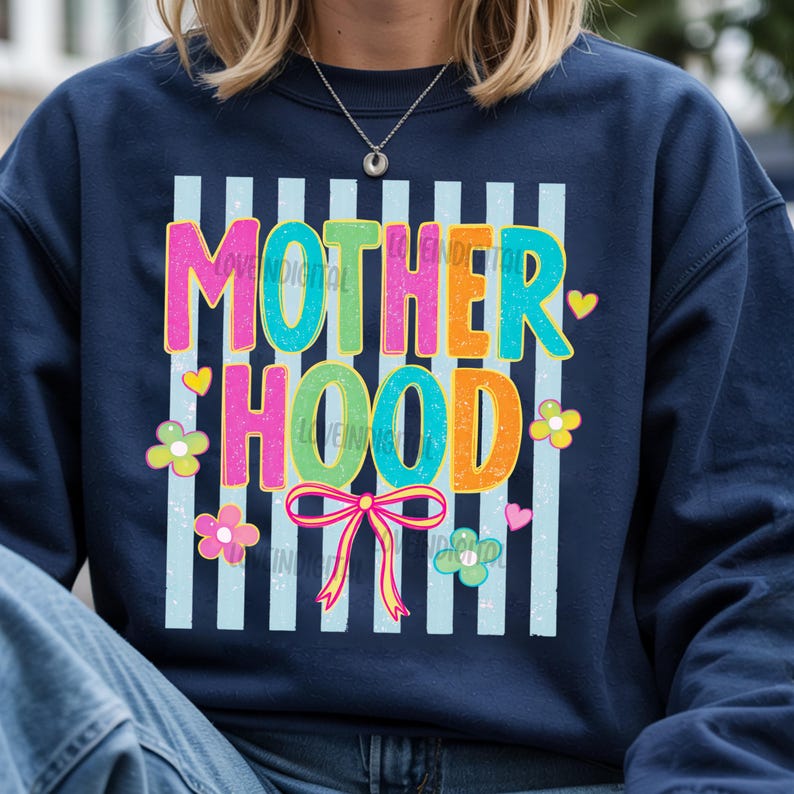 May include: Navy blue sweatshirt with the word "MOTHERHOOD" in colorful, bubble letters. The design includes vertical light blue stripes, flowers, hearts, and a bow. The text "LOVE DIGITAL" is also visible.