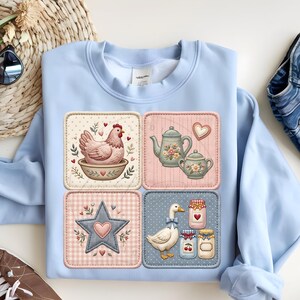 Puede incluir: Sudadera azul claro con cuatro parches cuadrados con ilustraciones campestres. Los parches representan una gallina, teteras, una estrella y un ganso con tarros de mermelada. El dise&ntilde;o incorpora corazones y detalles florales.