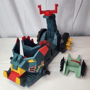 May include: A dark teal plastic toy vehicle featuring a red and yellow front bumper, a tall red top attachment, and black wheels with yellow accents. Beside the main vehicle sits a separate light green plastic component with black side pieces.