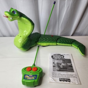 Puede incluir: Una cobra de juguete teledirigida de color verde con un patrón de escamas texturizado, lengua roja y ojos azules. Incluye un mando a distancia verde a juego con dos botones rojos y una antena larga, además de un manual llamado Slitherin' Tate.