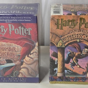 May include: Two Harry Potter audiobook cassette sets by J.K. Rowling, read by Jim Dale. The left box is Harry Potter and the Chamber of Secrets, and the right box is Harry Potter and the Sorcerer's Stone, both featuring colorful illustrations.