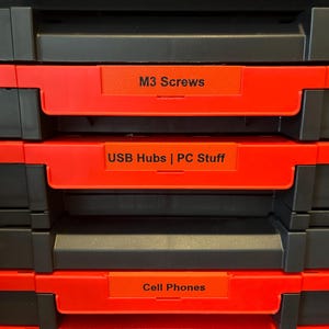 May include: A black and red storage box with three drawers. Each drawer has a white label with black text. The top drawer is labeled "M3 Screws", the middle drawer is labeled "USB Hubs | PC Stuff", and the bottom drawer is labeled "Cell Phones".