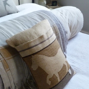 May include: A brown and beige throw pillow with a white silhouette of a horse. The pillow has a brown and white striped border.
