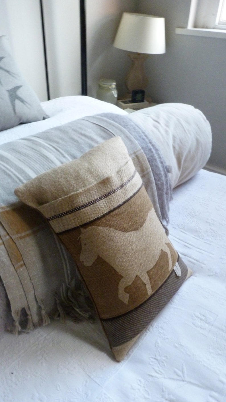 May include: A brown and beige throw pillow with a white silhouette of a horse. The pillow has a brown and white striped border.