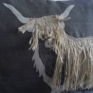 May include: A black and white pillow with a design of a Highland cow with long, shaggy hair. The cow's hair is a light brown color.