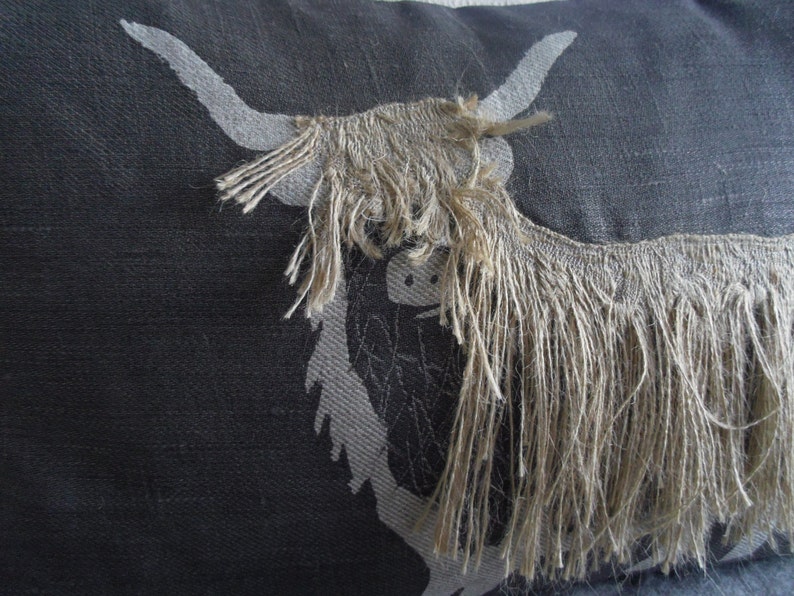 May include: A black and white pillow with a design of a Highland cow with long, shaggy hair. The cow's hair is a light brown color.