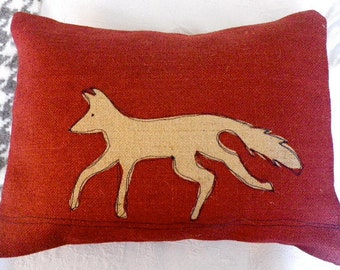 May include: A red pillow with a beige fox design. The fox is outlined in black and has a long tail.