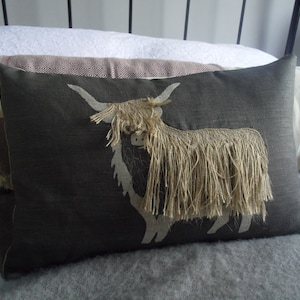 May include: A dark gray throw pillow with a white embroidered design of a Highland cow with long, shaggy hair.