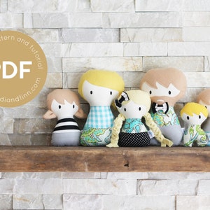 Op de afbeelding: Een set van zes handgemaakte stoffen poppen, waaronder een gezin van vier en twee baby's. De poppen zijn gekleed in verschillende patronen, waaronder ruitjes, bloemen en strepen. De poppen zijn gerangschikt op een houten plank tegen een witte bakstenen muur. De tekst "sewing pattern and tutorial PDF www.heidlandfinn.com" wordt in een cirkel op de muur weergegeven.
