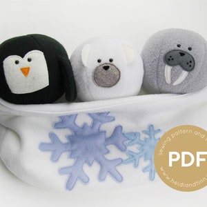 May include: Three plush stuffed animals, a penguin, a polar bear, and a walrus, are nestled in a white fleece fabric with a blue snowflake design. The fabric has a gold circle with the text "sewing pattern and tutorial PDF www.heidianfinn.com".