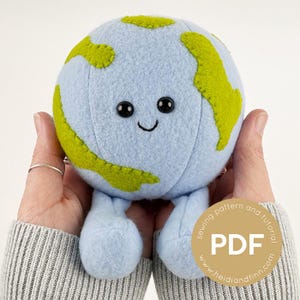 May include: A plush Earth toy with a smiling face, blue oceans, and green continents. The toy has black button eyes and small blue legs. A round sticker with the text "PDF" is visible.