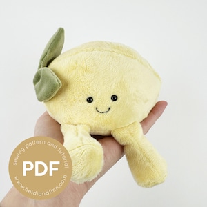 May include: A soft, yellow plush lemon toy with a smiling face, green leaf, and small legs. The toy has black embroidered eyes and a stitched mouth. The lemon is held in a hand, and a PDF logo is visible.