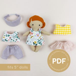 Può includere: Una bambola con i capelli rossi e un vestito floreale, circondata da vestiti e accessori per bambole. Il set include una fascia, pantaloncini, un top, una gonna e un top a quadretti gialli. Il testo "fits 5" dolls" è visibile.