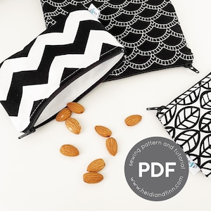 May include: Three black and white patterned zippered pouches with almonds scattered around them. One pouch has a chevron pattern, another has a scallop design, and the third has a leaf pattern. The pouches are open, revealing a white interior.